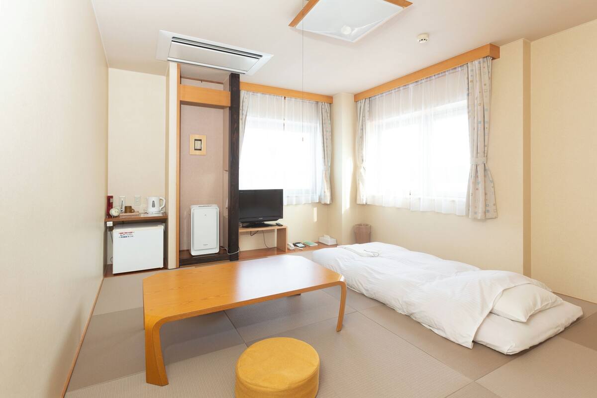 A hotel room with a bed, a desk, a television, a small refrigerator, and a window with curtains.