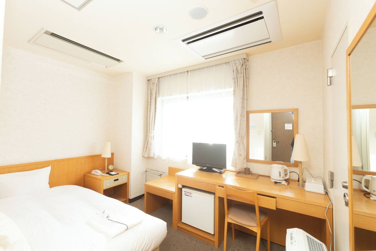 A hotel room with a bed, desk, chair, television, refrigerator, and a mirror.