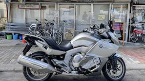 A BMW K1600 GT motorcycle parked outside a building with bicycles in the background. - Ezo House (Teshikaga)