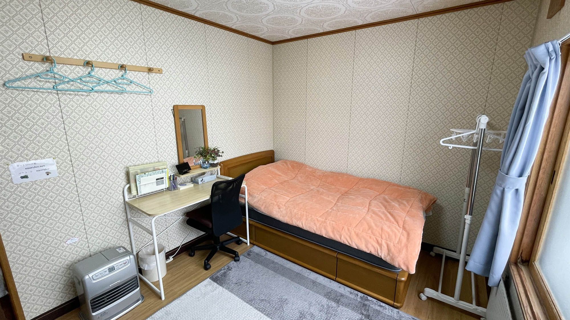 Una habitación pequeña y funcional con cama, escritorio, silla y radiador.