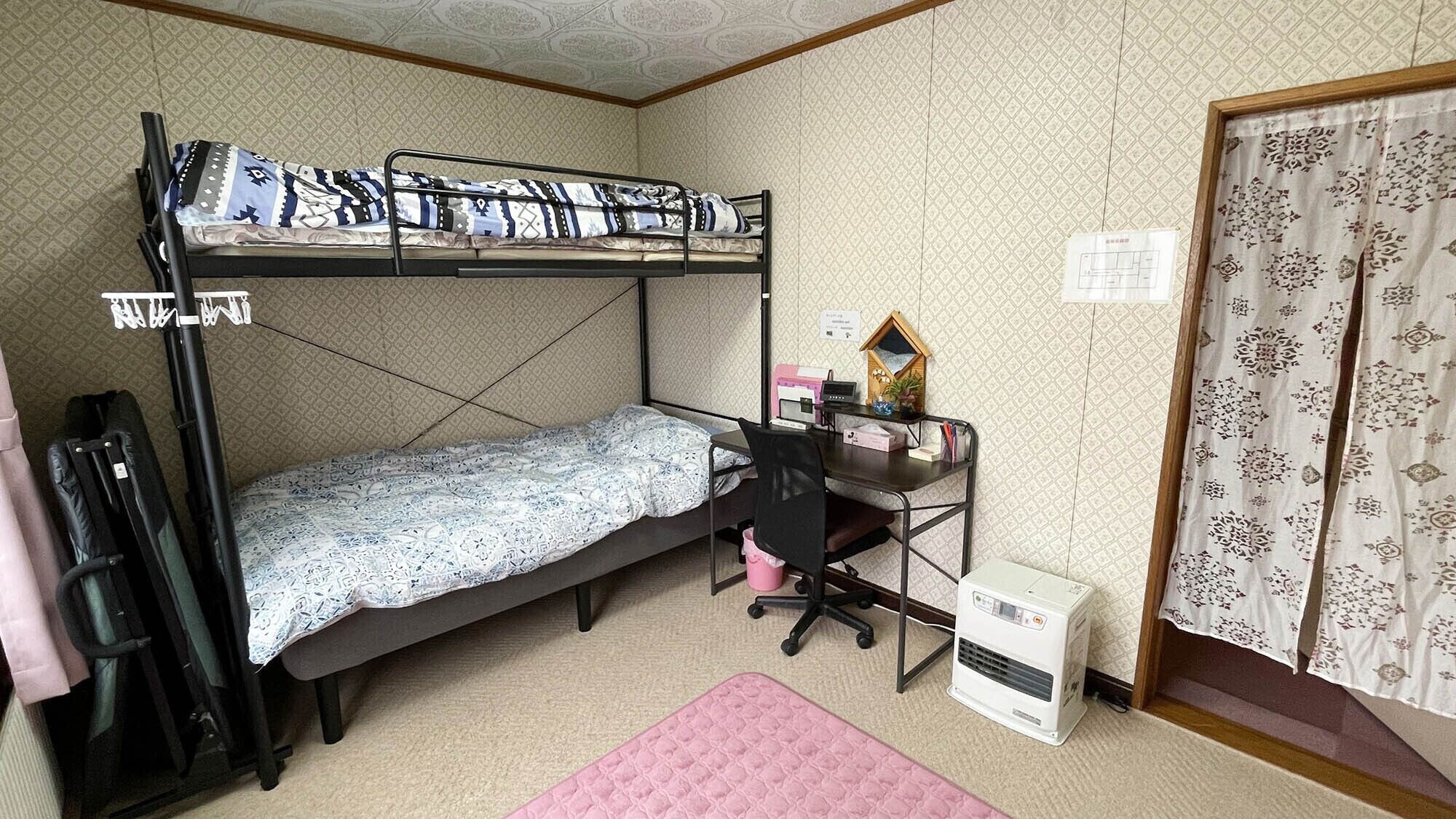 A dormitory room with bunk beds, a desk, a chair, a heater, and a curtain.
