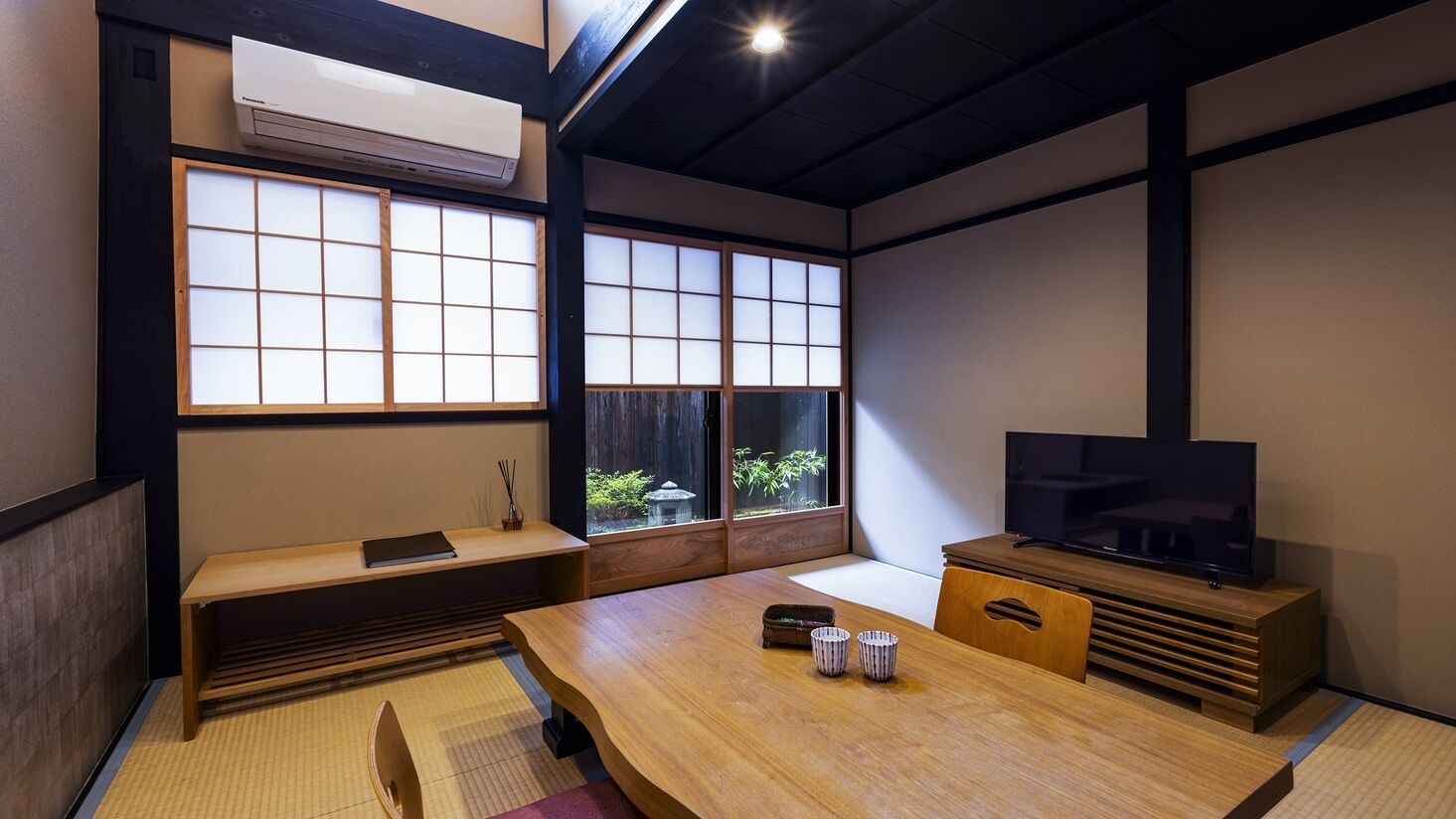Um quarto japonês tradicional, com tatames, uma mesa baixa, um banco, portas deslizantes e uma televisão.