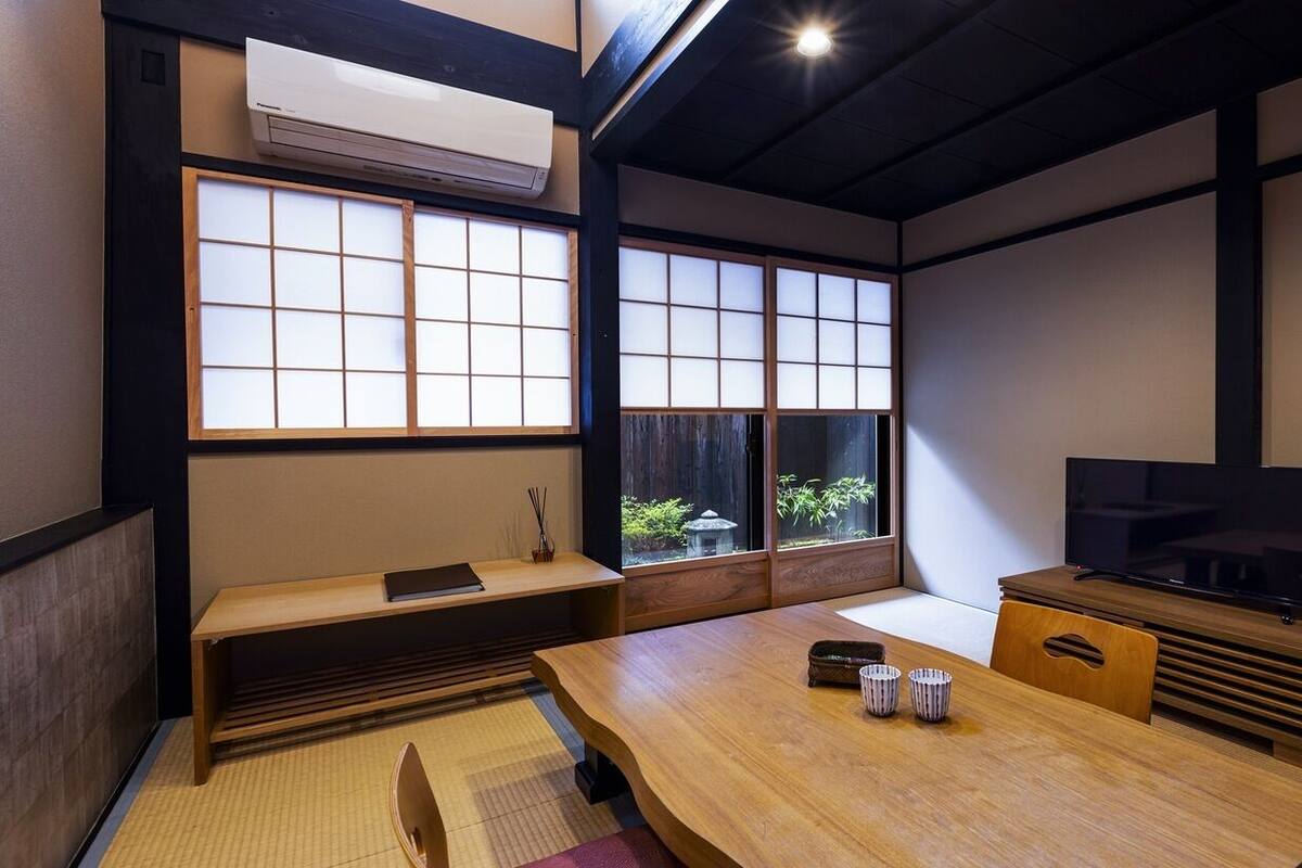 A traditional Japanese room with tatami flooring, a low table, a bench, sliding doors, and a television.