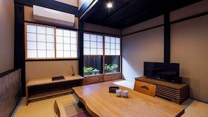 Una habitación japonesa tradicional con suelo de tatami, una mesa baja, un televisor y puertas correderas shoji.
