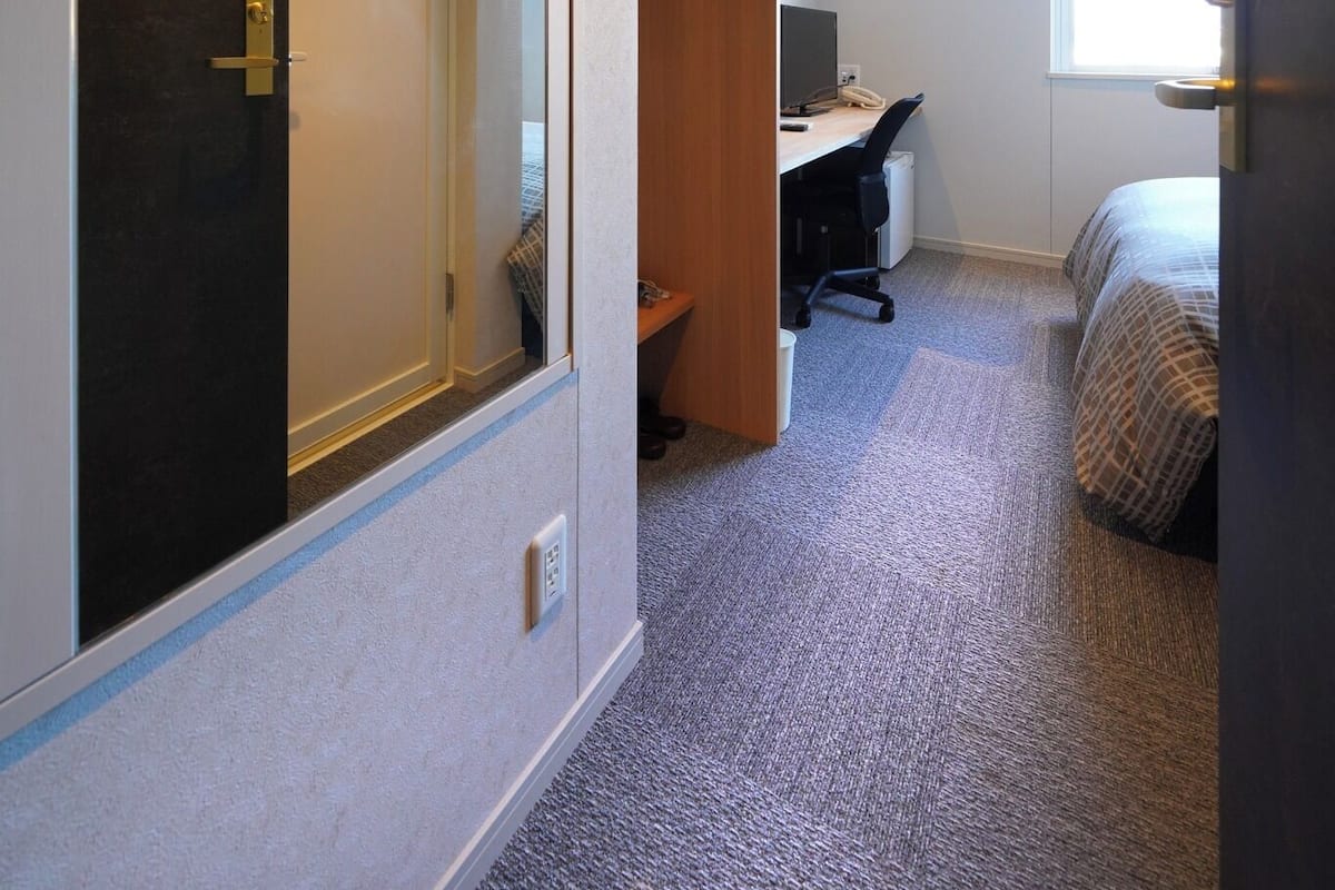A hotel room with a bed, a desk, a chair, a wardrobe, and a mirror.