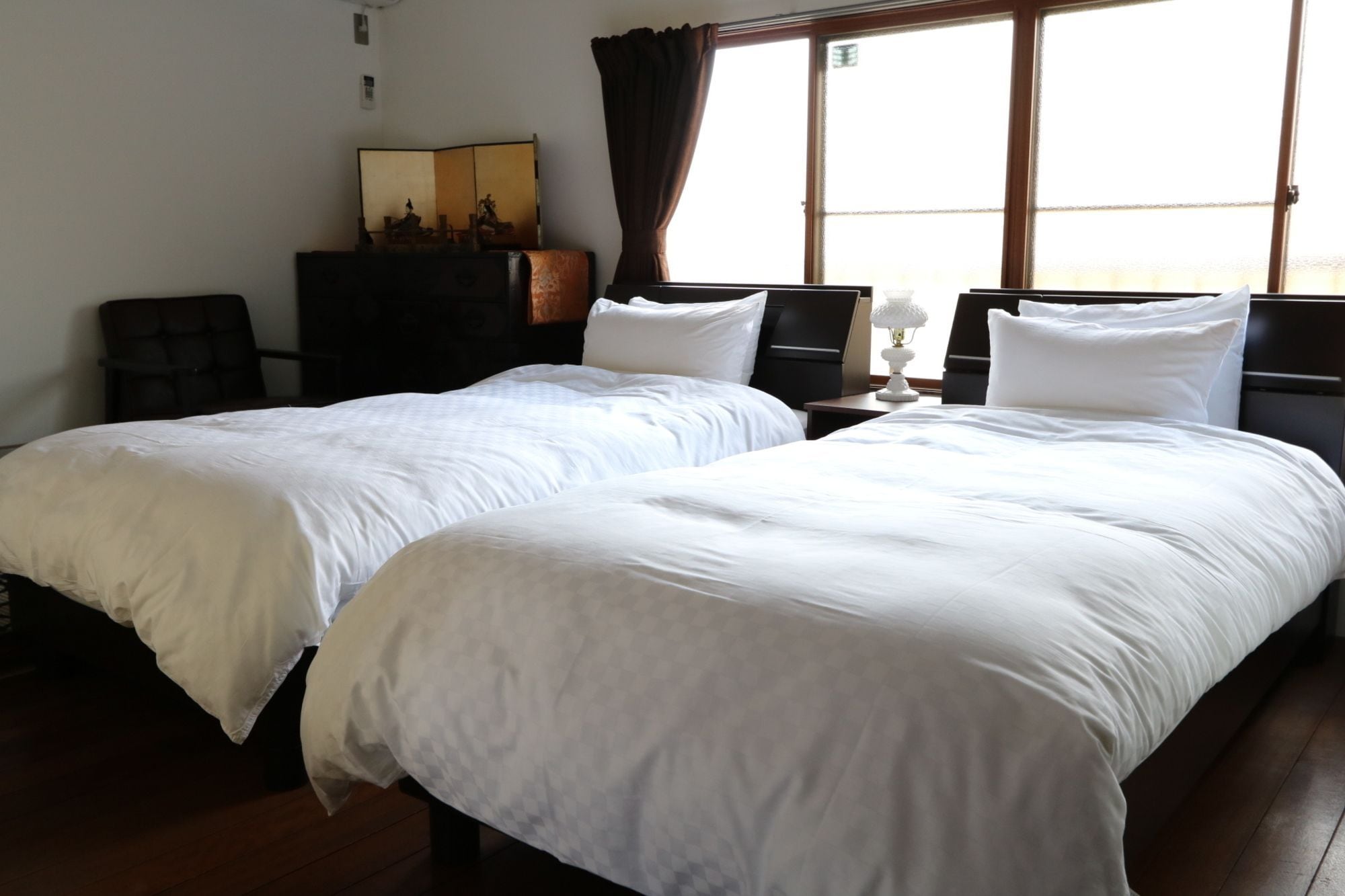 A hotel room with two single beds, a desk, a chair, a dresser, and a window with curtains.