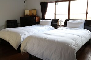 A hotel room with two single beds, a desk, a chair, a dresser, and a window with curtains. - Satsukian (Kyoto)