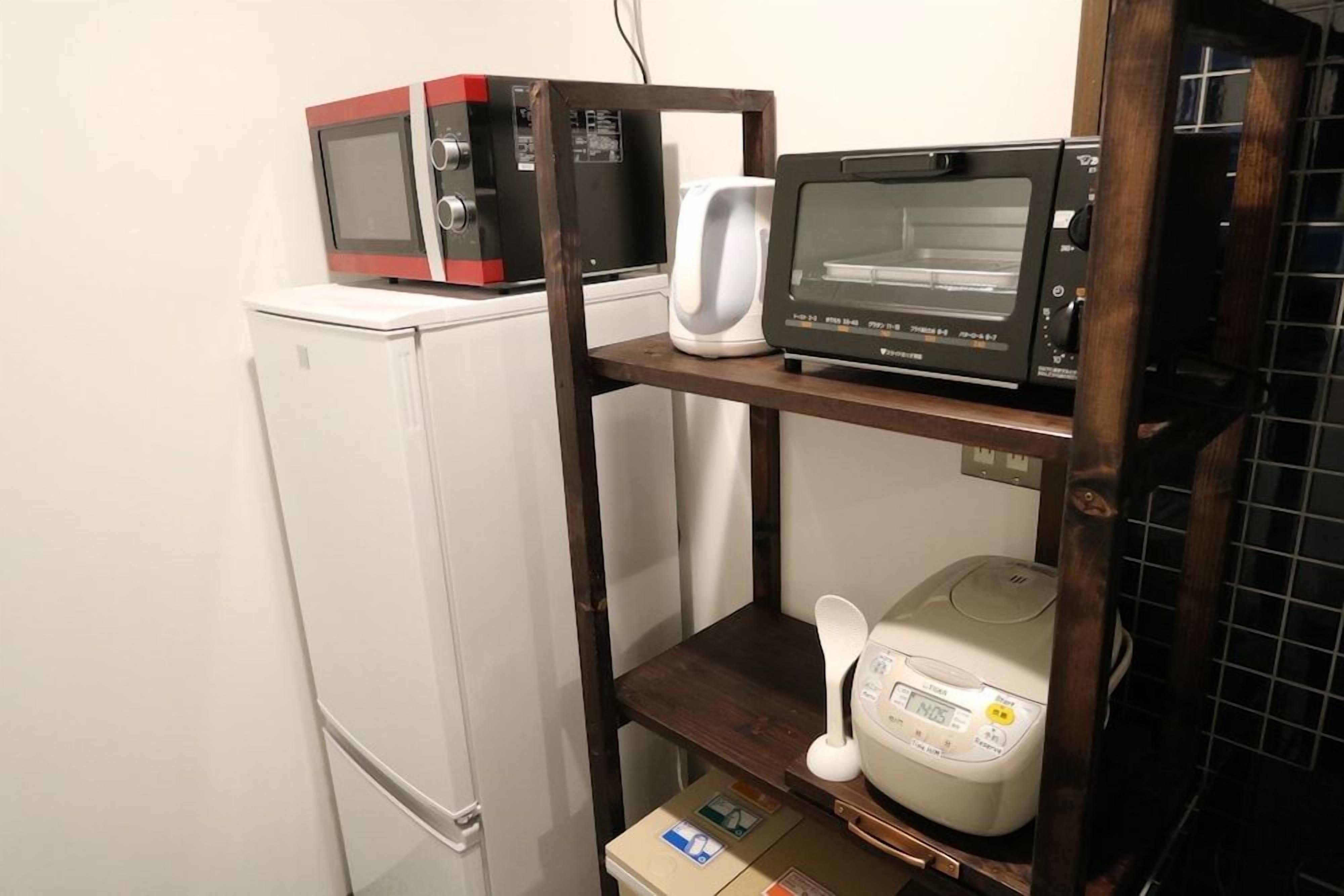 A kitchen with a microwave, toaster, and rice cooker on shelves, and a refrigerator.