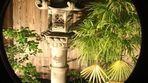 A stone lantern with intricate carvings, surrounded by lush green plants and a wooden fence. - Satsukian (Kyoto)