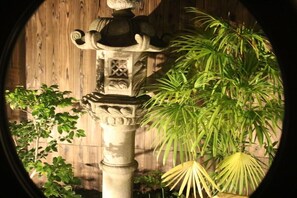 A stone lantern with intricate carvings, surrounded by lush green plants and a wooden fence. - Satsukian (Kyoto)