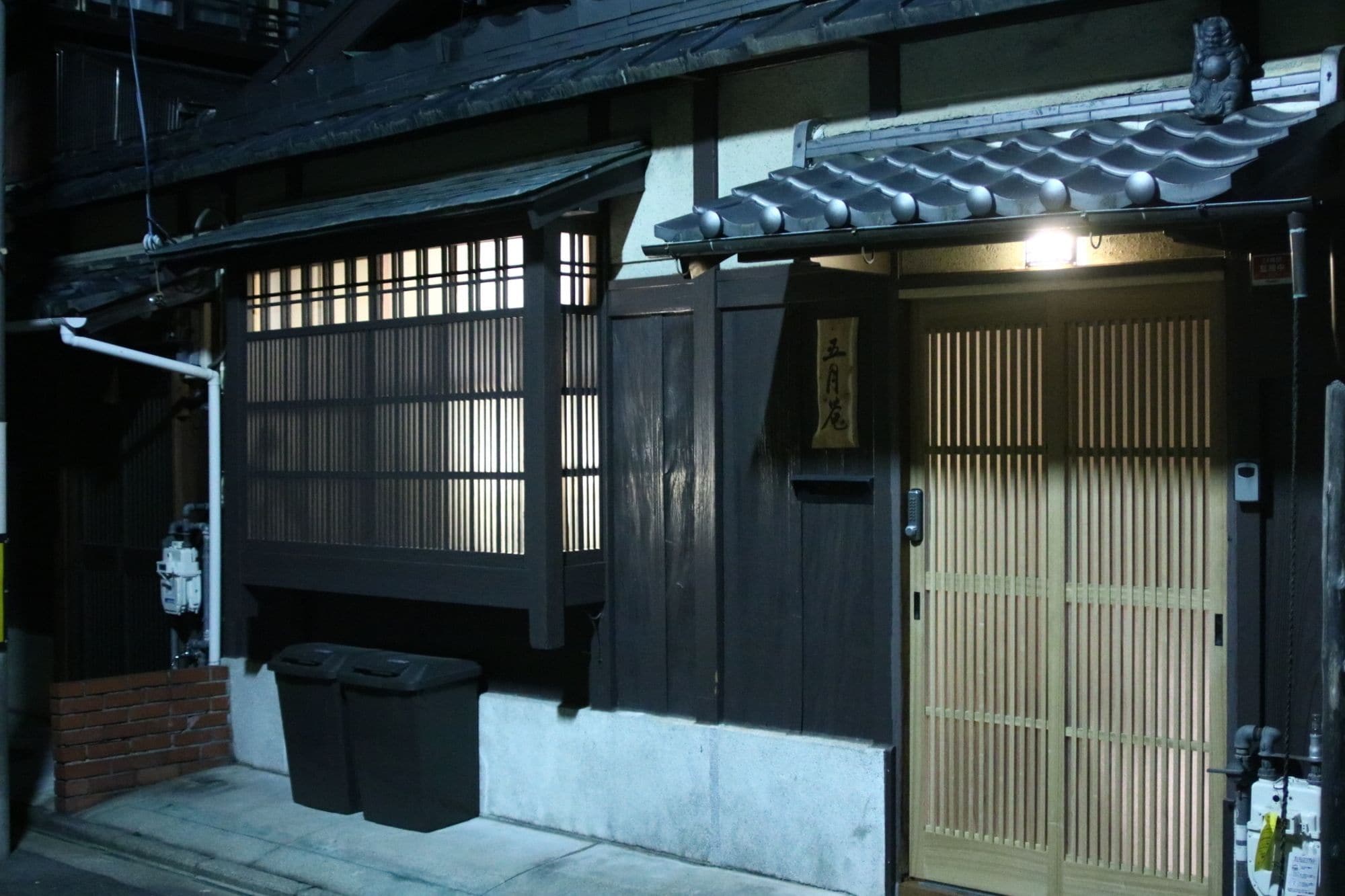 A traditional Japanese building with a wooden door, a sliding gate, and a small trash bin outside.