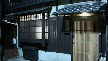 A traditional Japanese building with a wooden door, a sliding gate, and a small trash bin outside.