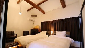 Quarto de hotel com duas camas, vigas de madeira, uma escrivaninha e uma cadeira.