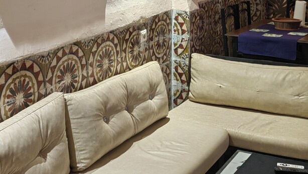 Una sala de estar con un sofá color beige, un papel tapiz estampado y obras de arte enmarcadas.