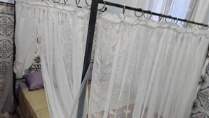 Un dormitorio con cama con dosel, dosel, piso de madera y ventana con cortinas.