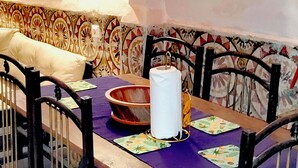 Un comedor con una mesa dispuesta para cuatro personas, rodeada de sillas, una pared con diseño y una estantería con objetos decorativos.