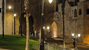 Una calle iluminada por farolas, con una palmera y un edificio histórico con arcos.