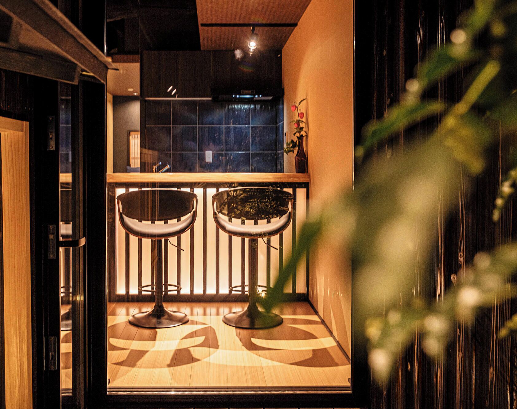 Una zona de bar con dos taburetes, una planta en maceta y vistas a la cocina.