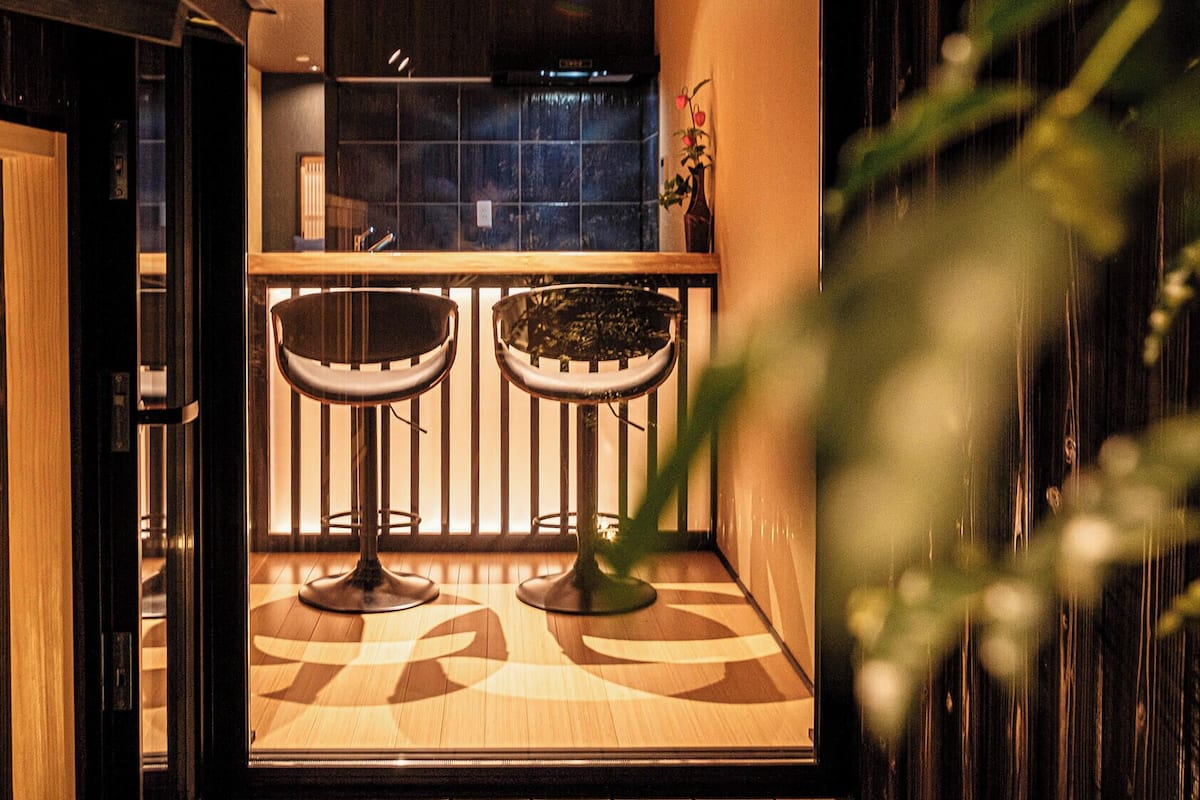 Una zona de bar con dos taburetes, una planta en maceta y vistas a la cocina.