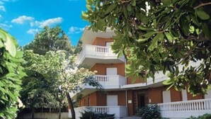 A multi-story building with a white balcony, surrounded by greenery. - Cozy Apartment 3min From the Beach (Lignano Sabbiadoro)