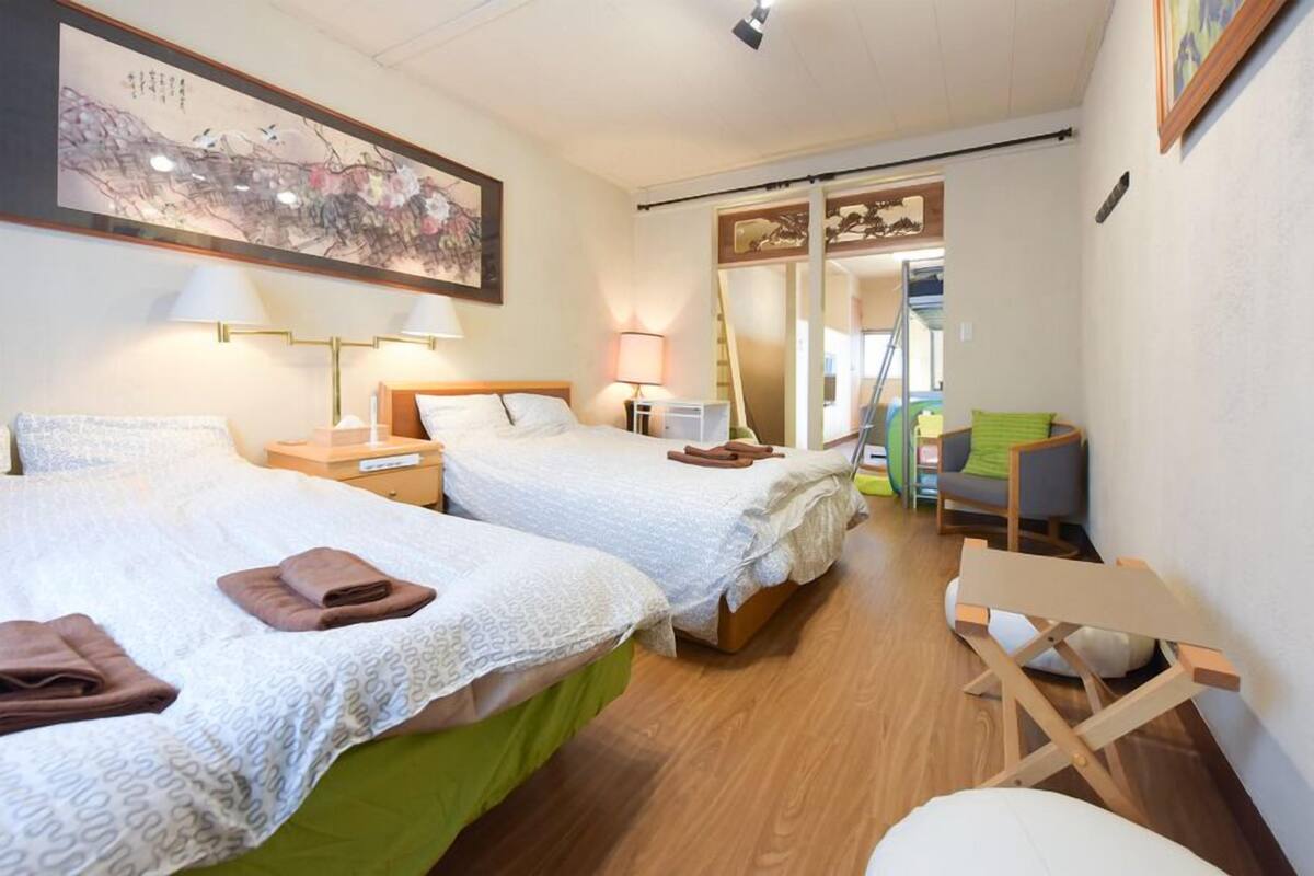 A hotel room with two beds, a desk, a chair, and a large painting on the wall.