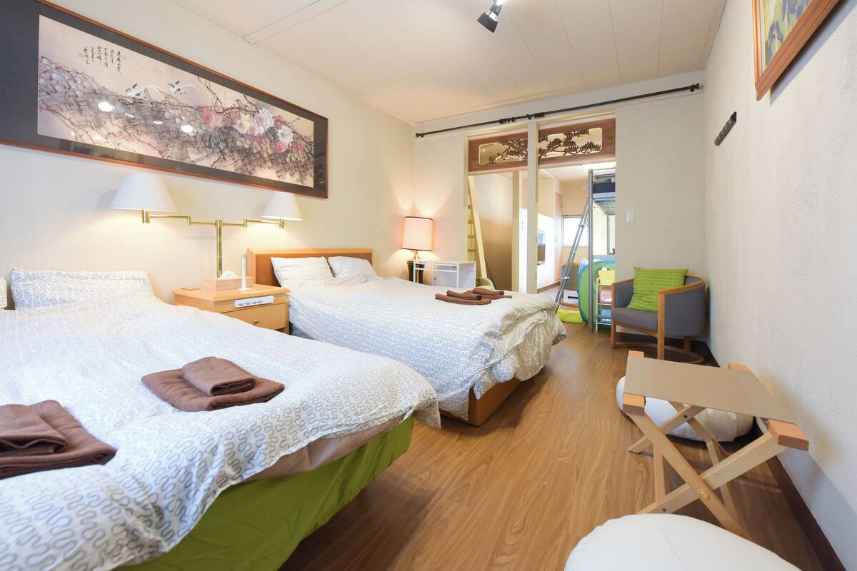 A hotel room with two beds, a desk, a chair, and a sliding door leading to a balcony.