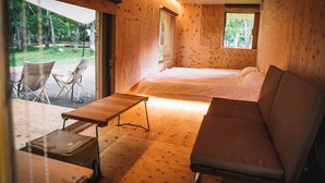 A wooden cabin interior with a bed, a sofa, a table, and a chair. - Akaigawa Tomo Playpark Jubako (Akaigawa)