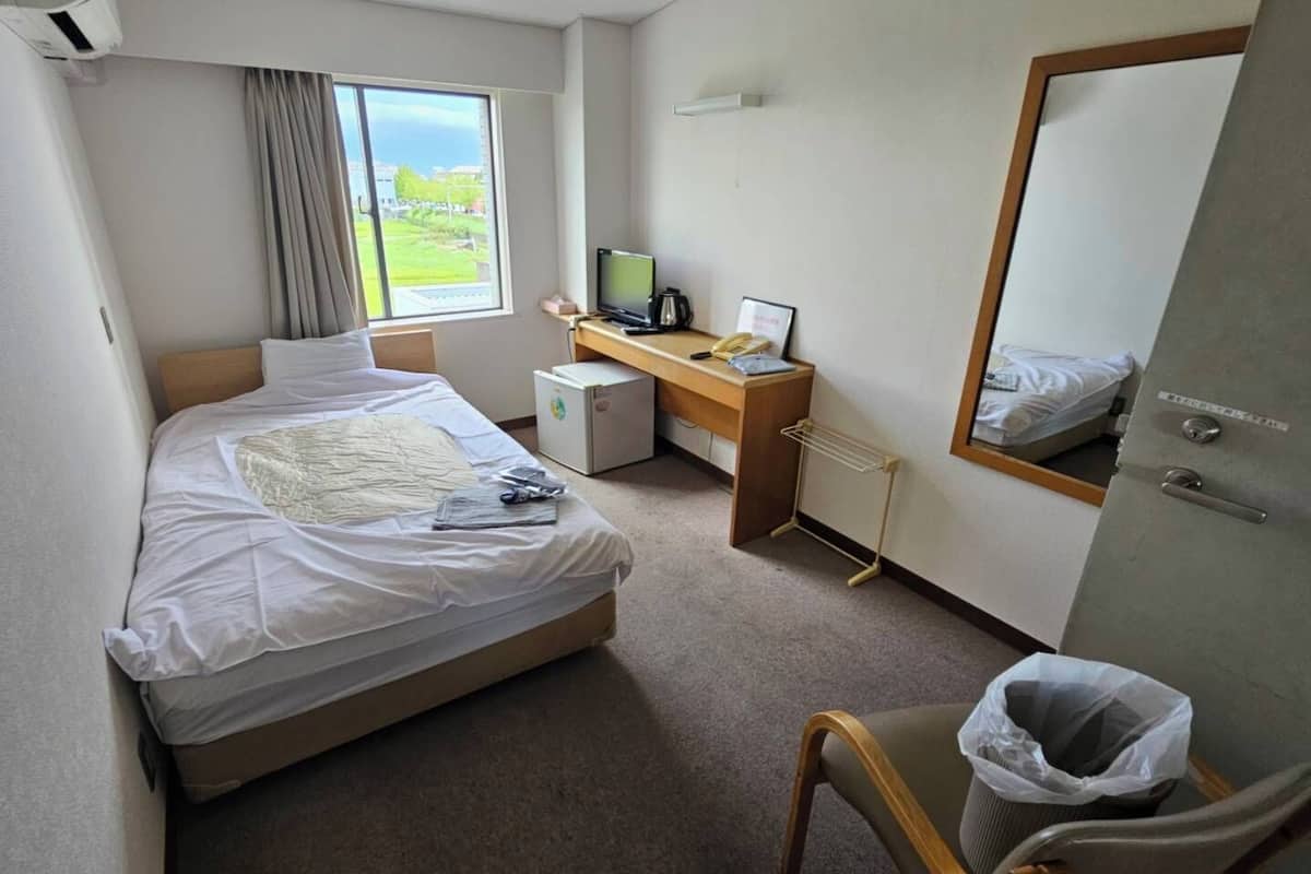 A hotel room with a bed, a desk, a computer, a mirror, and a view of the outdoors.