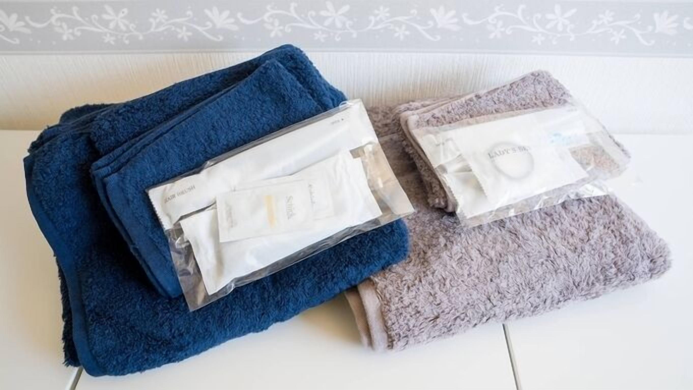 A room with a white wall and a patterned border, a blue towel, and a grey towel.