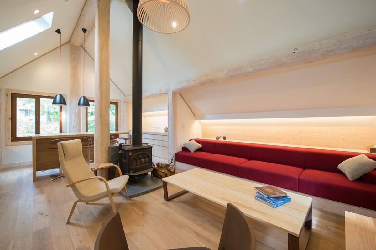 Una sala de estar acogedora con un sofá rojo, una mesa de madera, una chimenea y un ventanal grande.