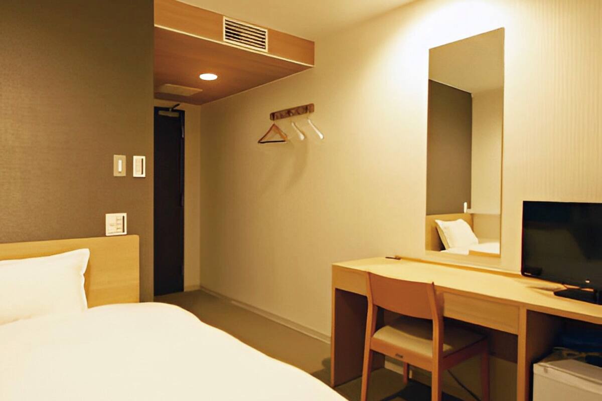 A hotel room with a bed, a desk with a chair, a television, and a mirror.