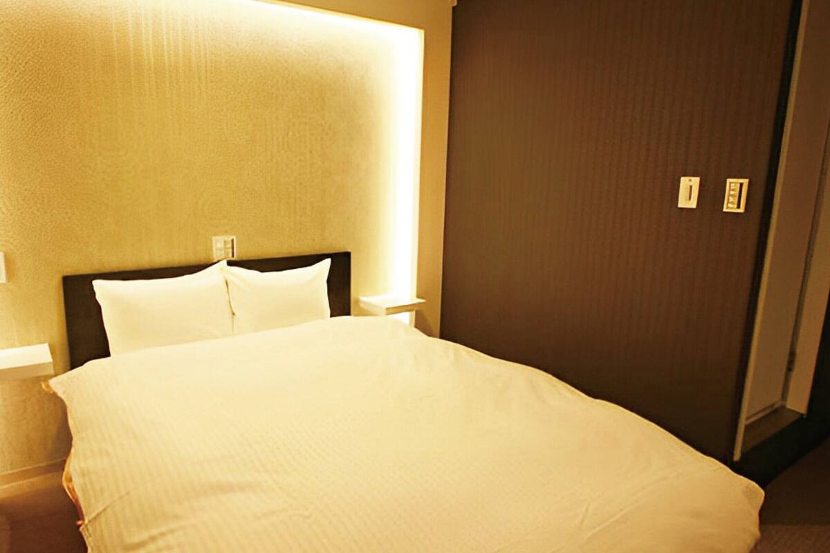 A hotel room with a large bed, a nightstand, a wall-mounted light, and a door with a lock.