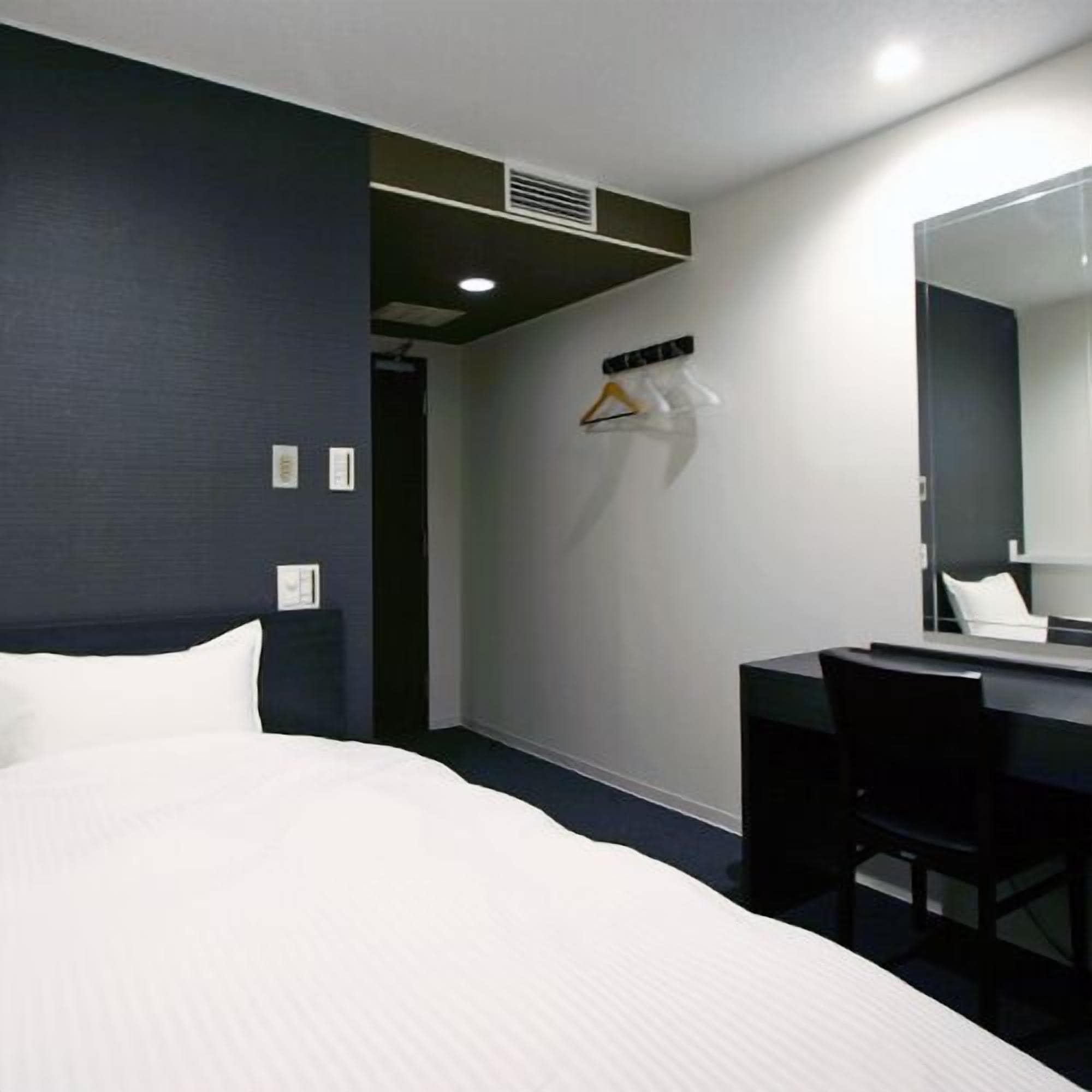 A hotel room with a bed, a desk, a chair, a mirror, and a coat rack with hangers.