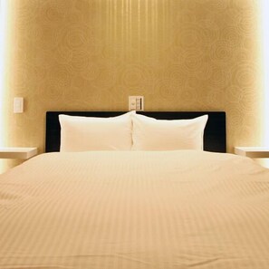 Una cama bien hecha con un cabecero negro, almohadas blancas y una colcha color beige en una habitación con papel tapiz estampado.