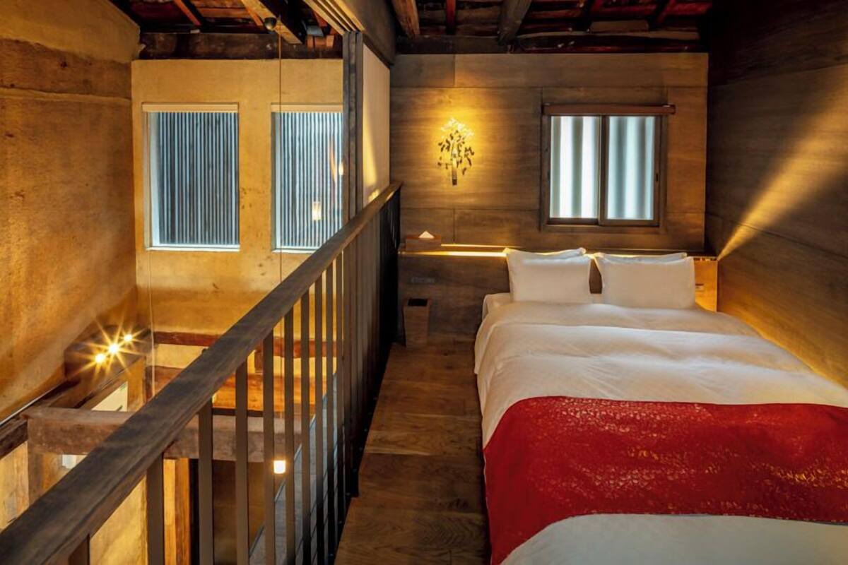 A bedroom with a wooden ceiling, a bed with white linens, a red throw blanket, and a wall-mounted light fixture.