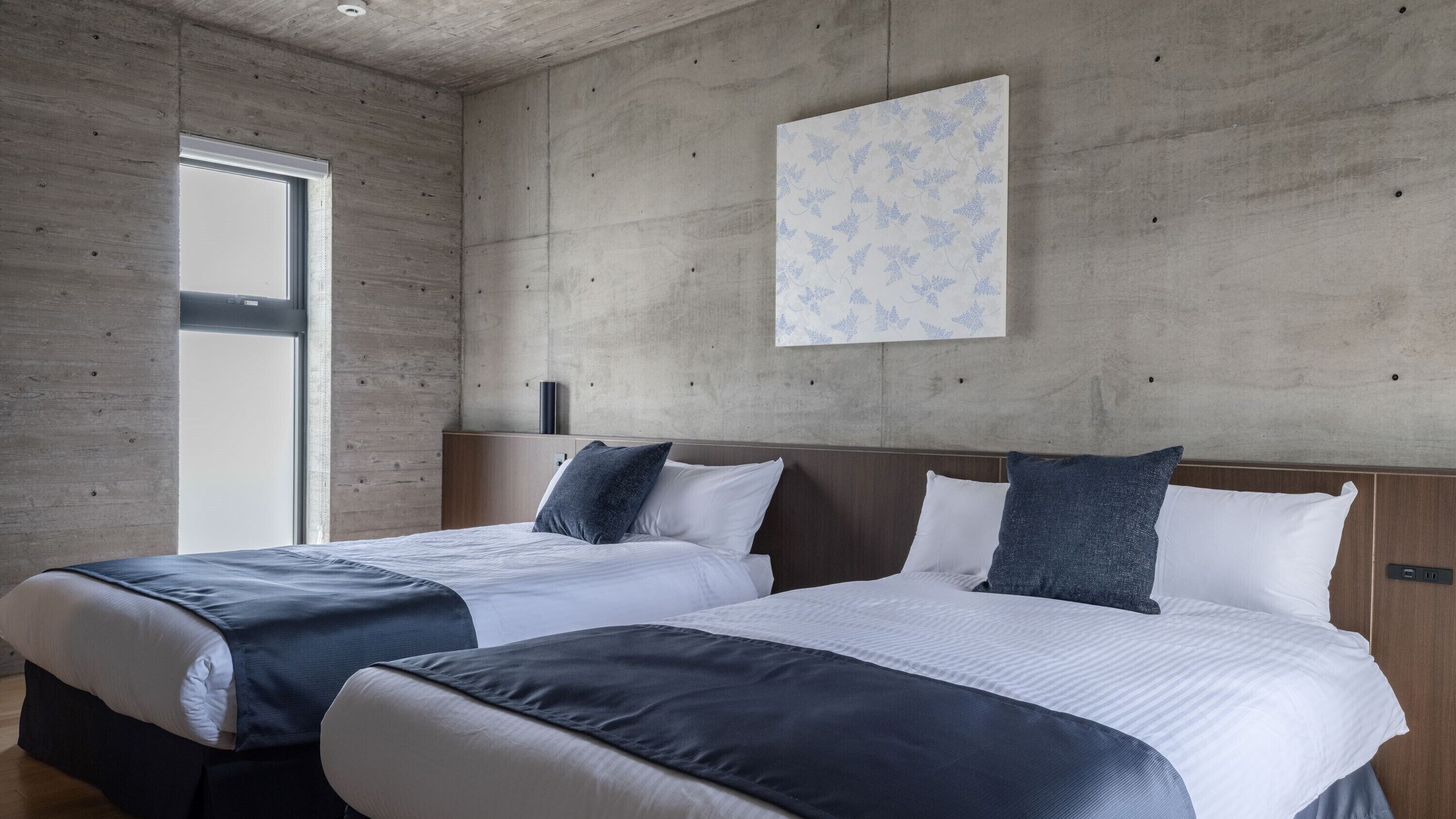 Une chambre d’hôtel moderne avec deux lits, une grande fenêtre et un mur en béton agrémenté d’un panneau décoratif.
