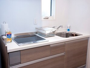 A modern kitchen with a built-in induction cooktop, a stainless steel sink, and a window above the sink. - Vicoletto Inn Hakata Sumiyoshi (Fukuoka)