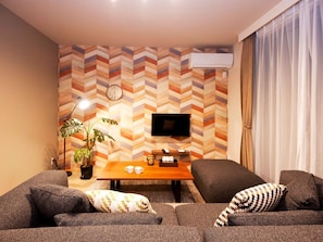 A living room with a sofa, a coffee table, a TV, and a clock on the wall. - Vicoletto Inn Hakata Sumiyoshi (Fukuoka)