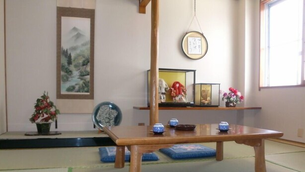 Ein traditioneller japanischer Raum mit Tatami-Boden, einem niedrigen Holztisch und einem Regal mit Dekorationen.
