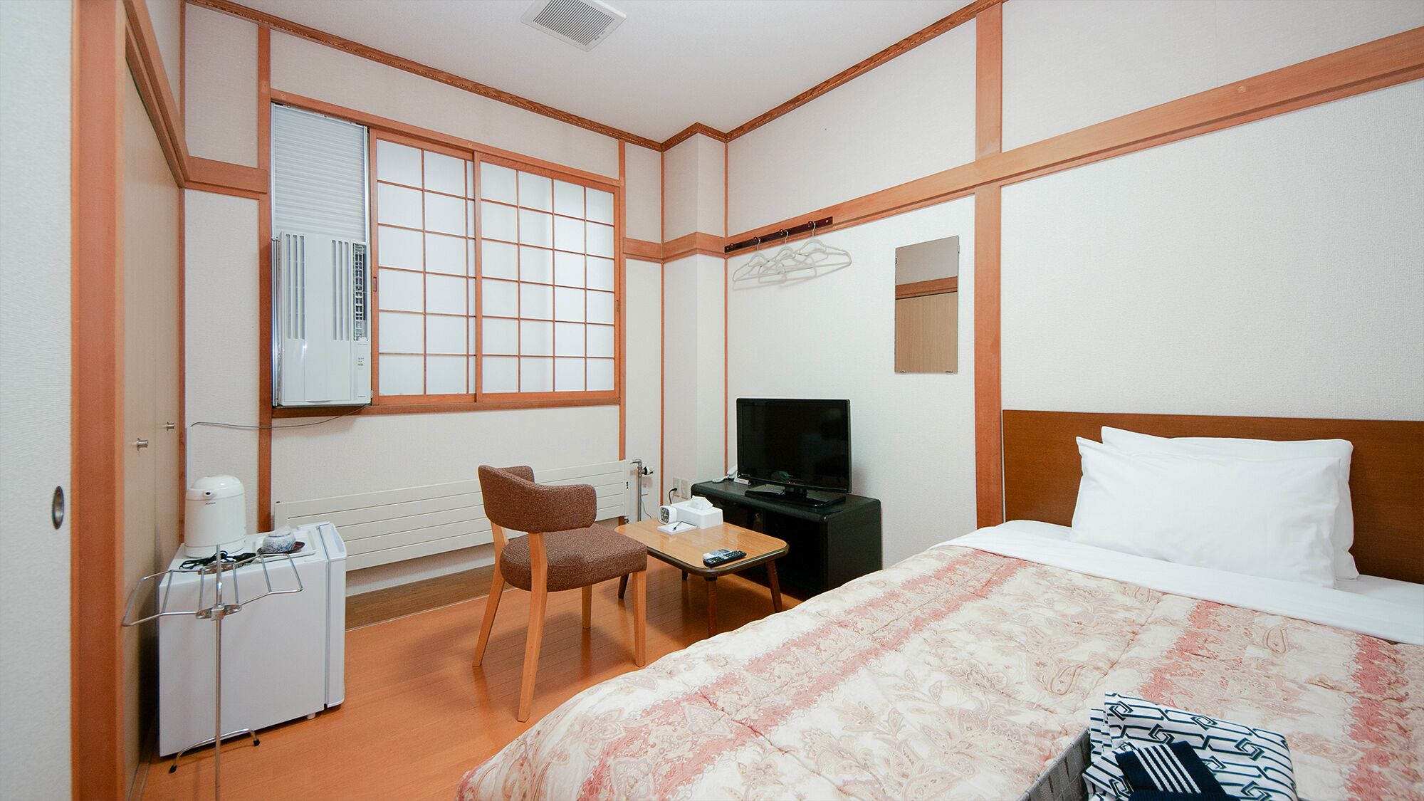 A hotel room with a bed, a desk, a chair, a television, a radiator, and a window with a view.
