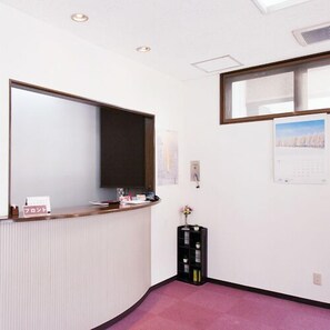 A reception area with a reception desk, a black storage unit, a wall-mounted calendar, and a window with a view. - Yojo Ryokan (Nayoro)