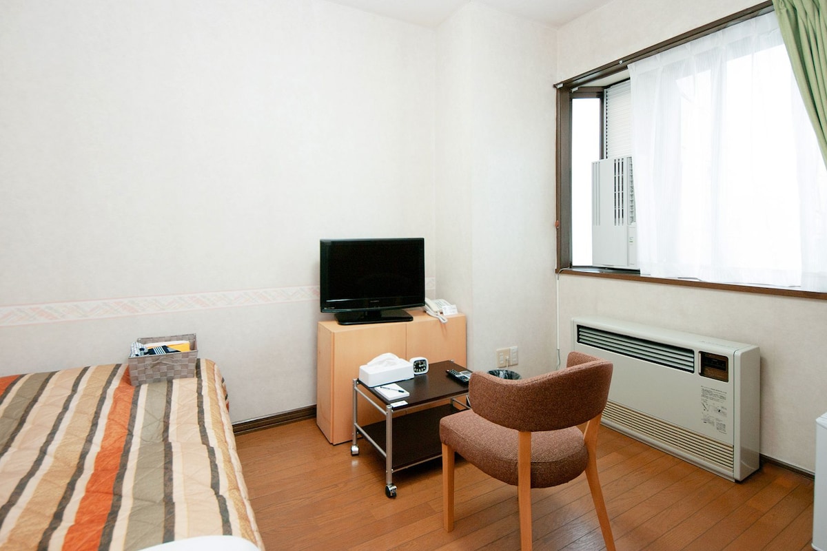 A hotel room with a bed, a desk with a television, a chair, and a radiator.