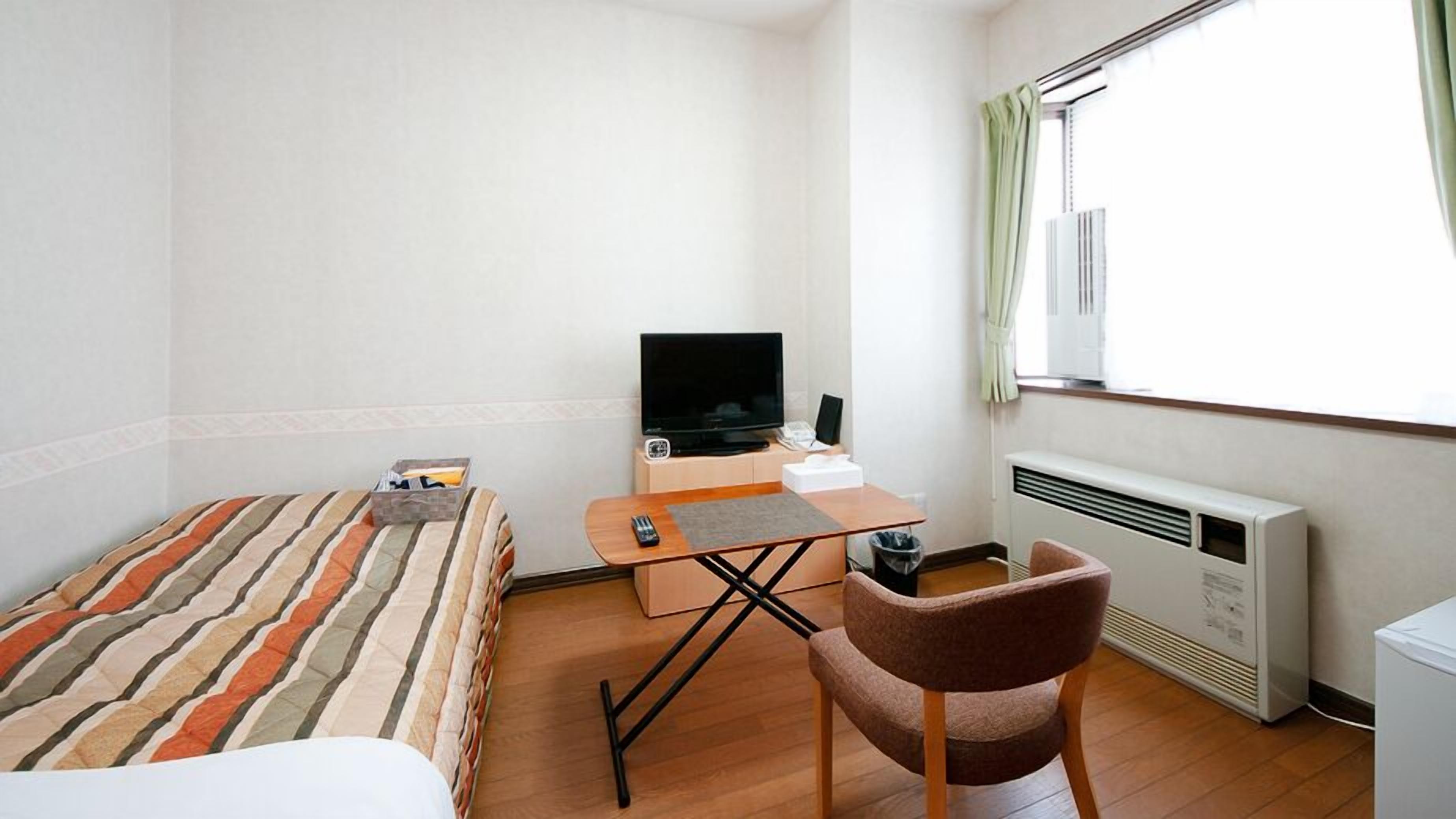 A hotel room with a bed, a desk with a television, a chair, and a radiator.
