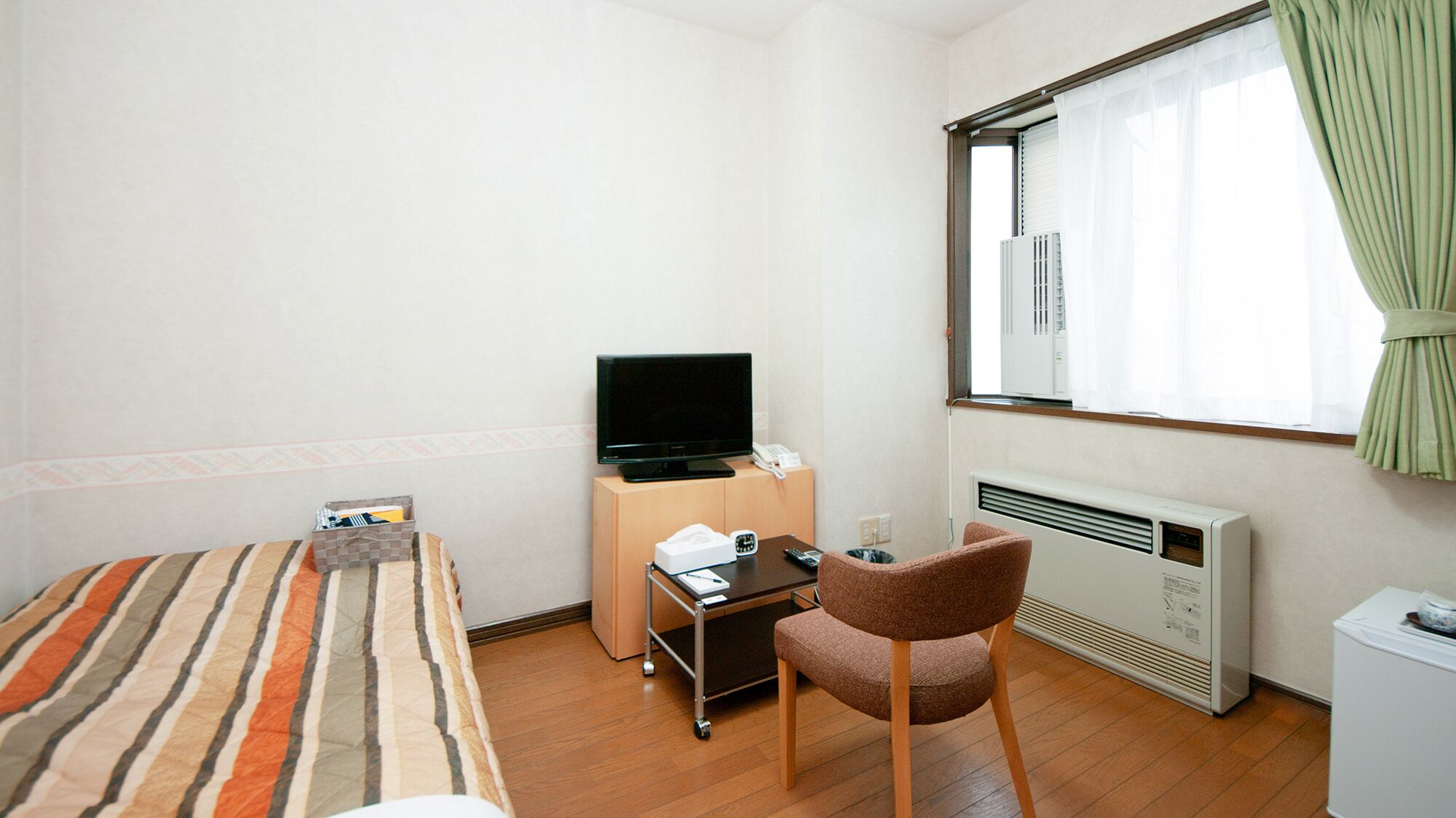 A hotel room with a bed, a desk with a television, a chair, and a radiator.