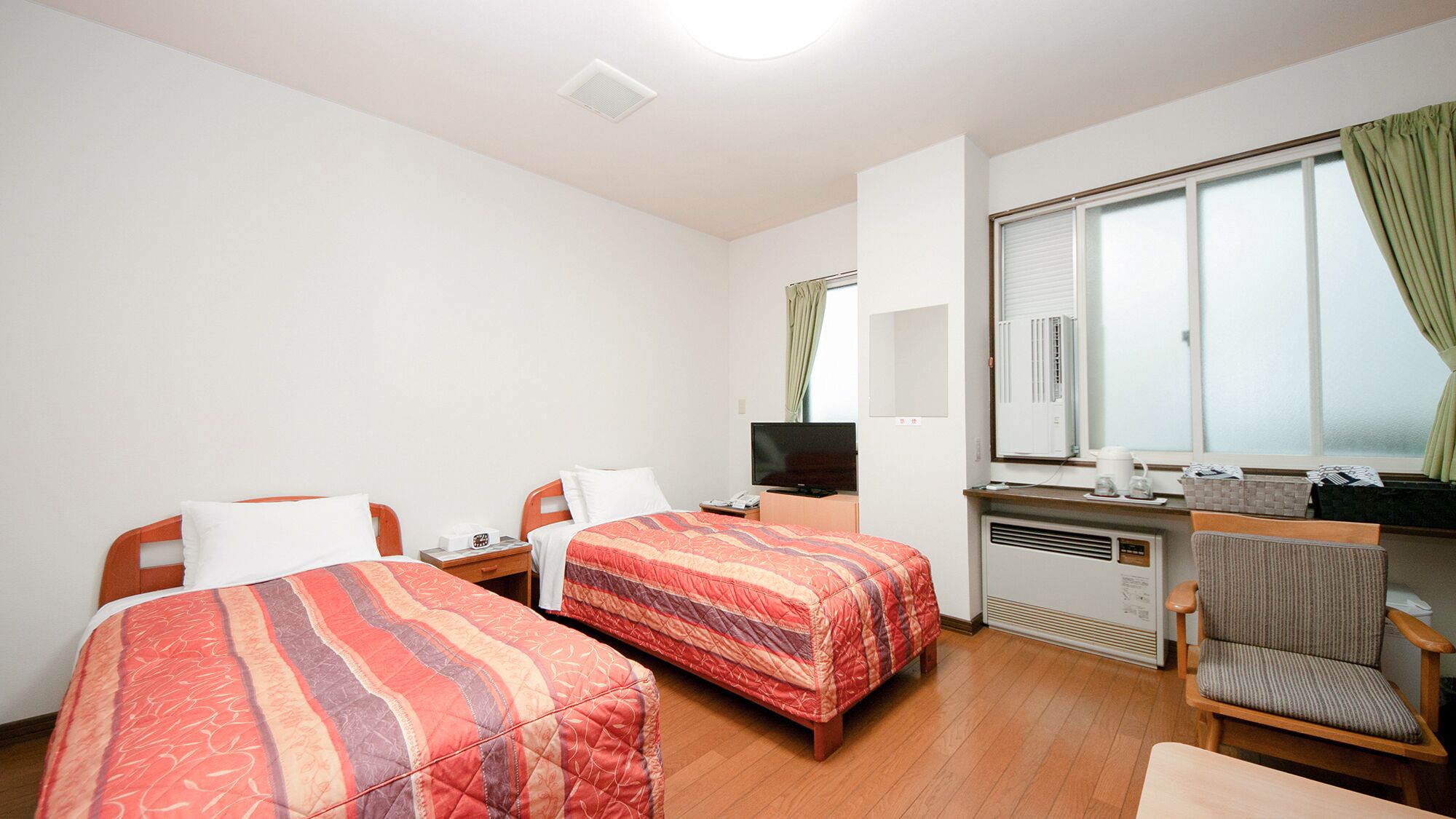 A hotel room with two beds, a TV, a desk with a computer, a chair, and a window with curtains.