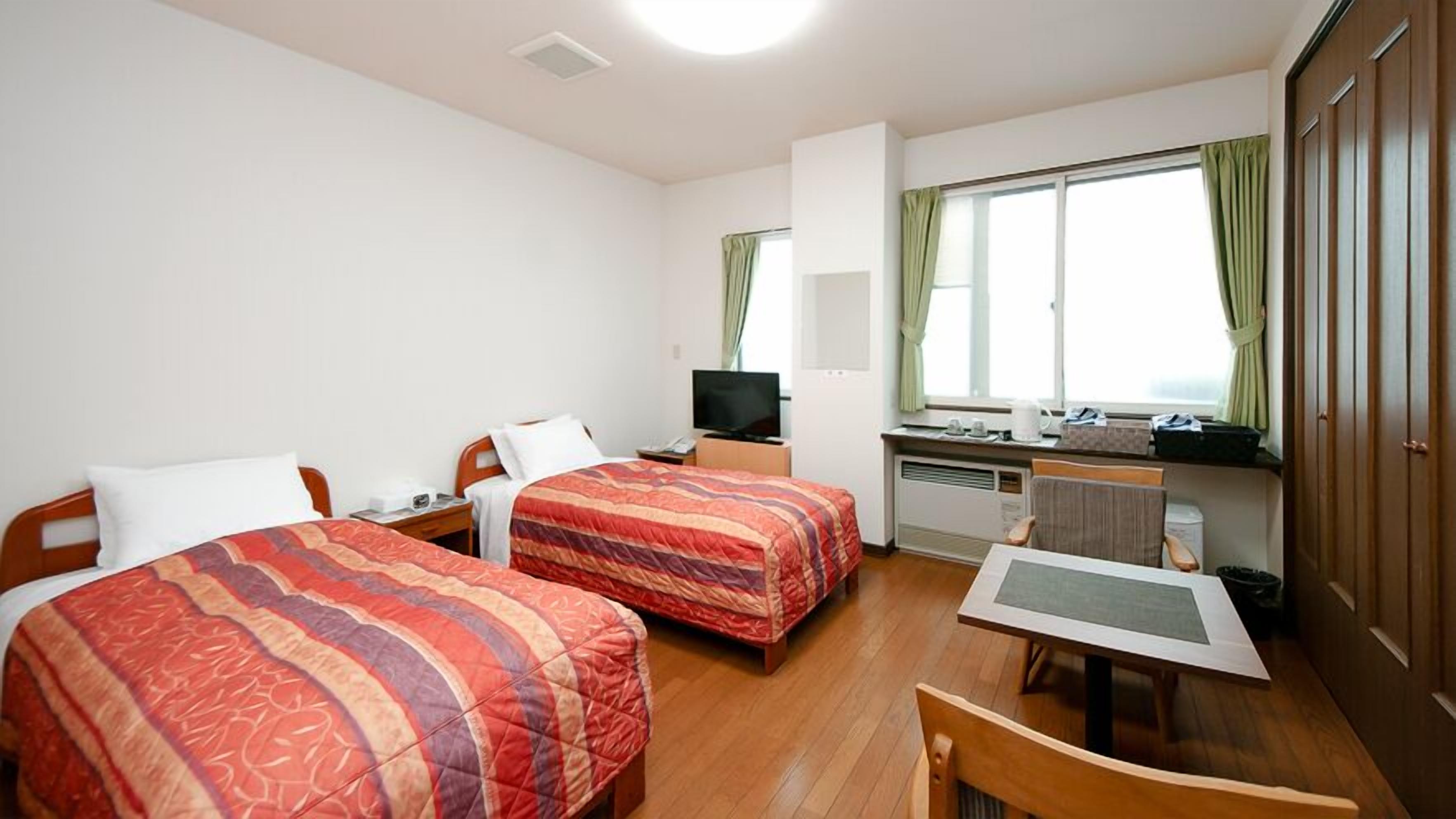 A hotel room with two beds, a desk, a chair, a television, and a window with curtains.
