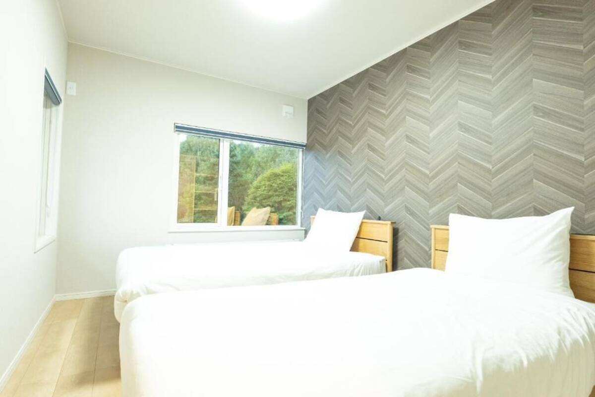 A bedroom with two beds, a window, and a herringbone-patterned wall.