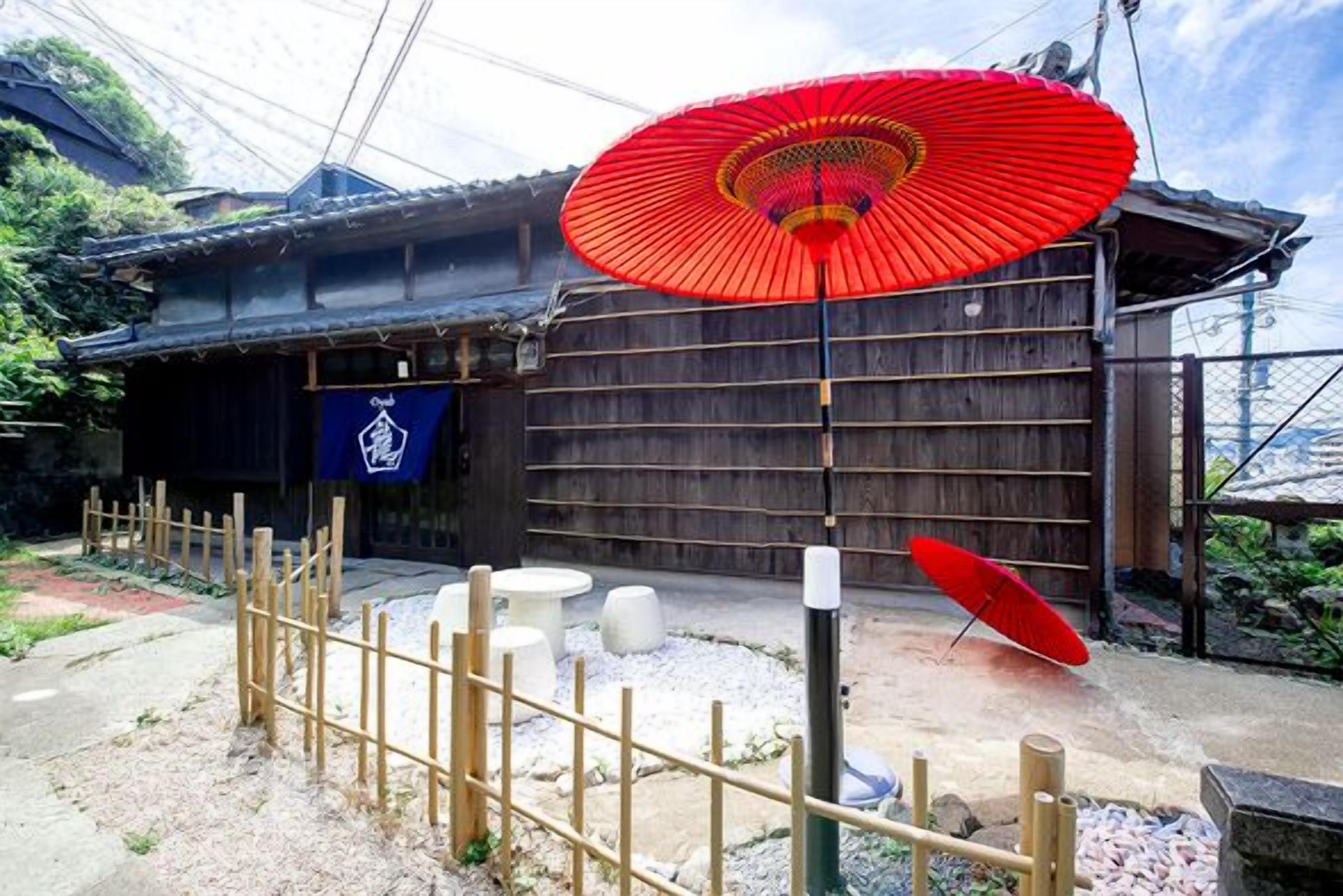 Un bâtiment traditionnel japonais, avec une clôture en bois, un parapluie rouge et une lanterne en pierre.