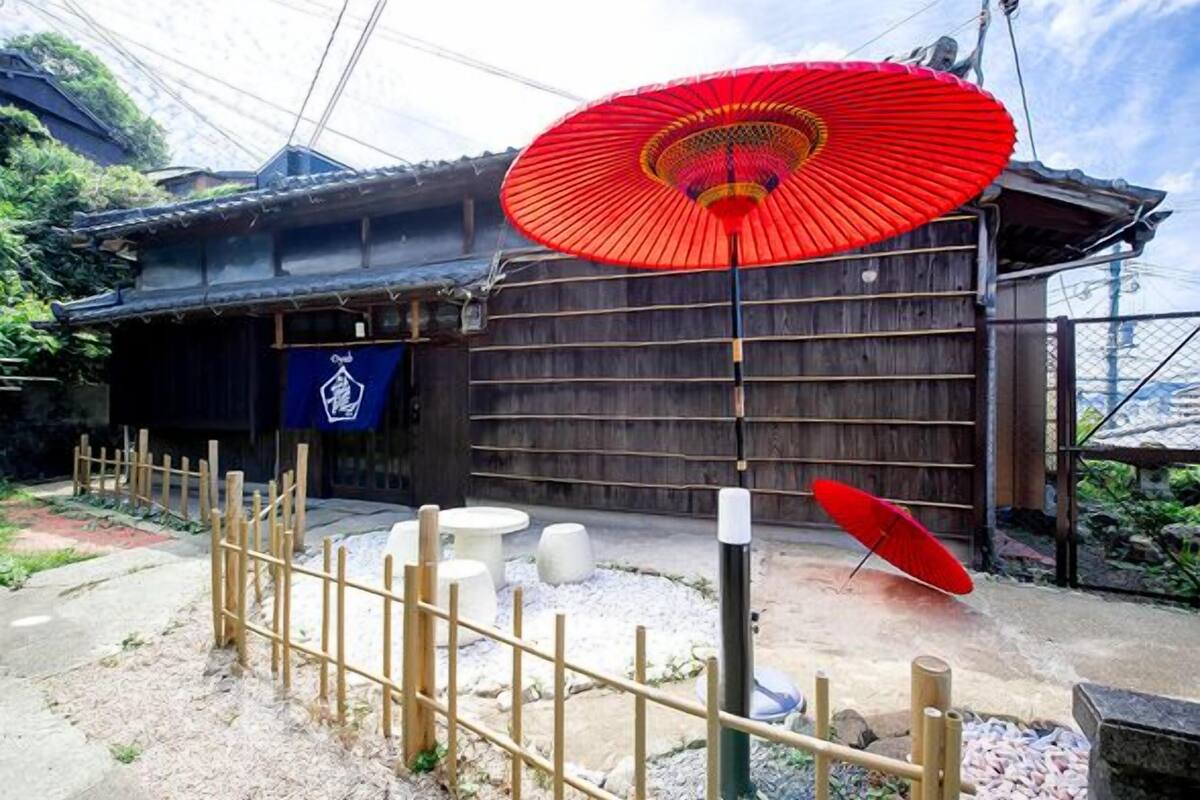 A traditional Japanese building with a wooden fence, a red umbrella, and a stone lantern.