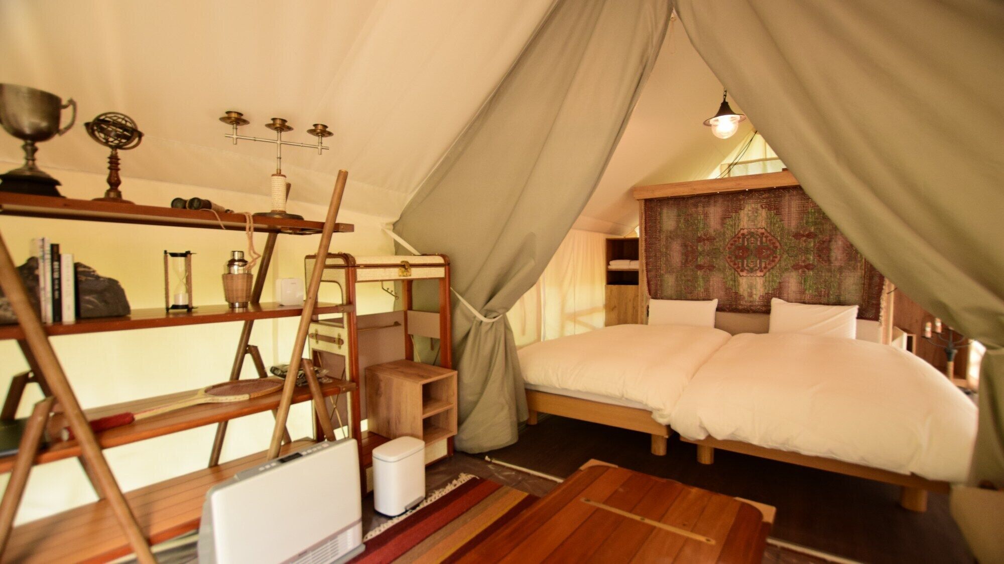 Um quarto aconchegante em estilo de tenda, com cama, estantes com livros e objetos decorativos, uma mesinha e um lustre suspenso.